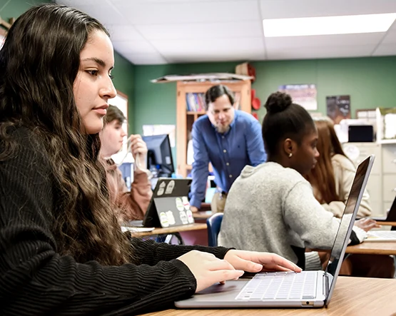 Female in black shirt on computer. Teacher in blue in background